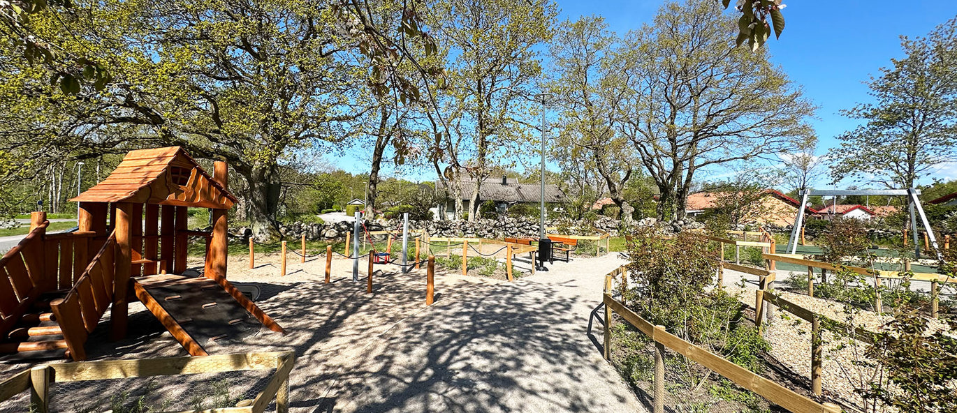 Lekplats i en park med planteringar, grusgångar och lekredskap.