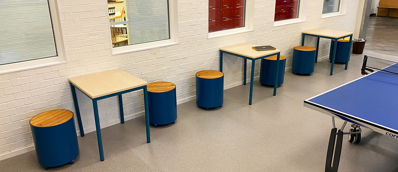 Flera blåa pallar med träsits samt bord och ett bordtennisbord på en skola.