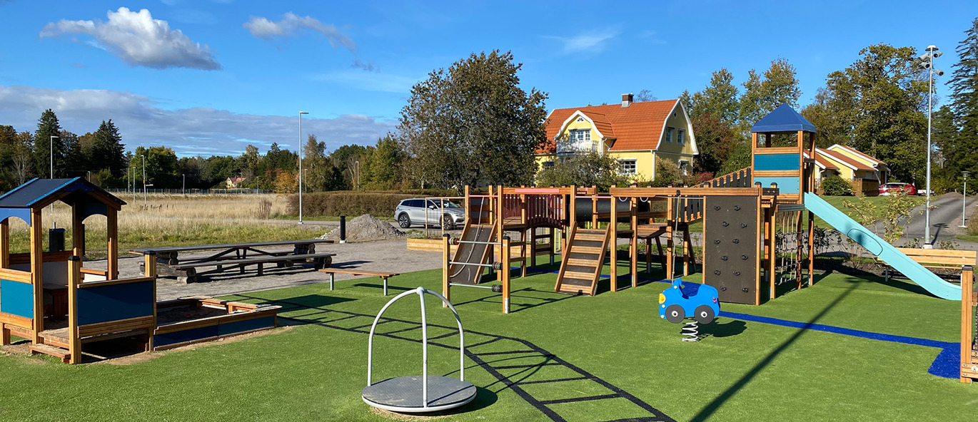 Lekplats med grönt konstgräs och färgglada lekställningar, lekredskap och sandlåda.