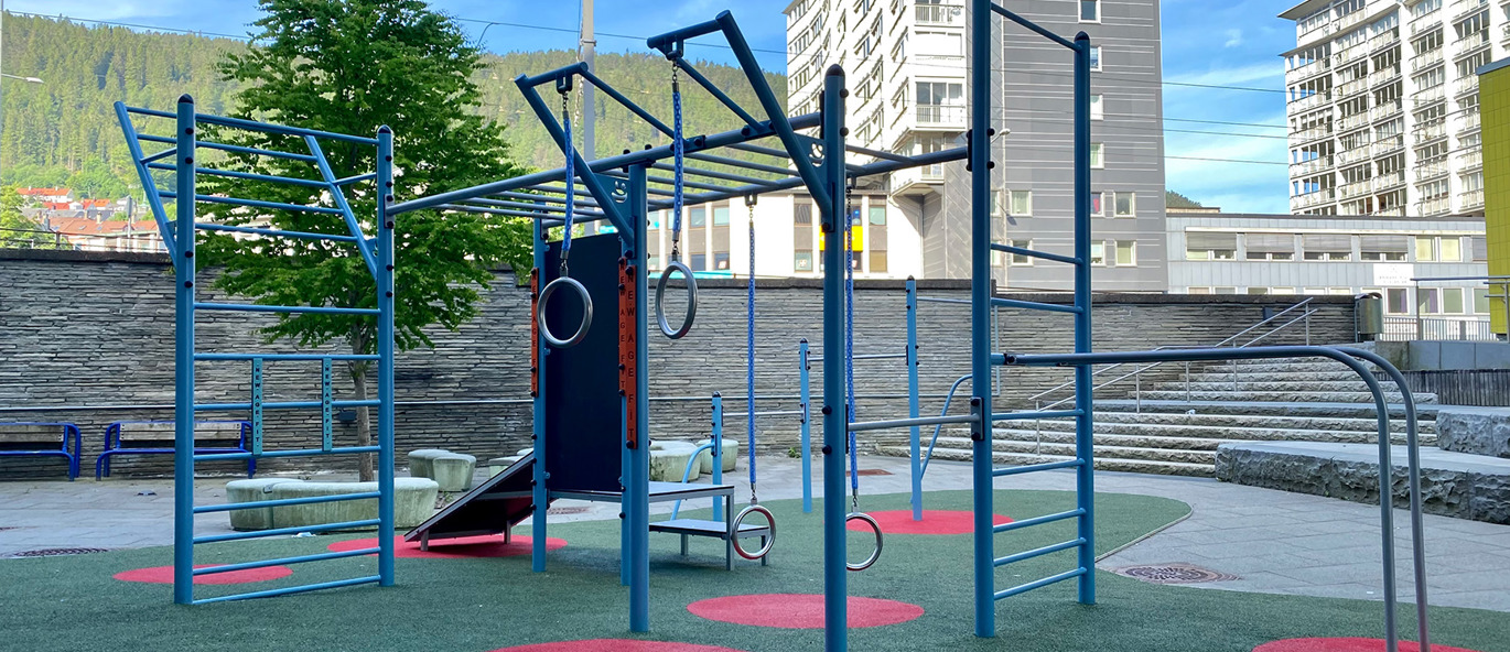 Blå träningsställning med färgglatt gummiunderlag och bostadshus o bakgrunden.