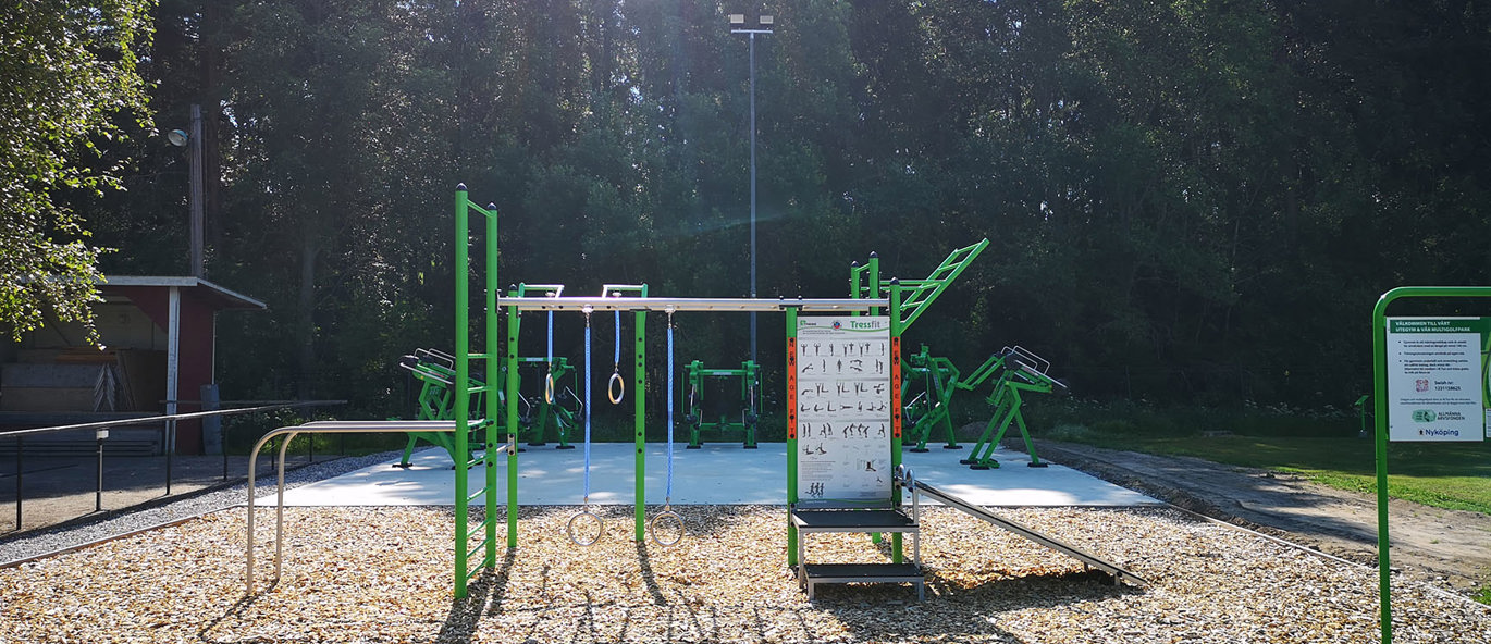 Grön träningsställning med gröna träningsmaskiner och skog i bakgrunden.