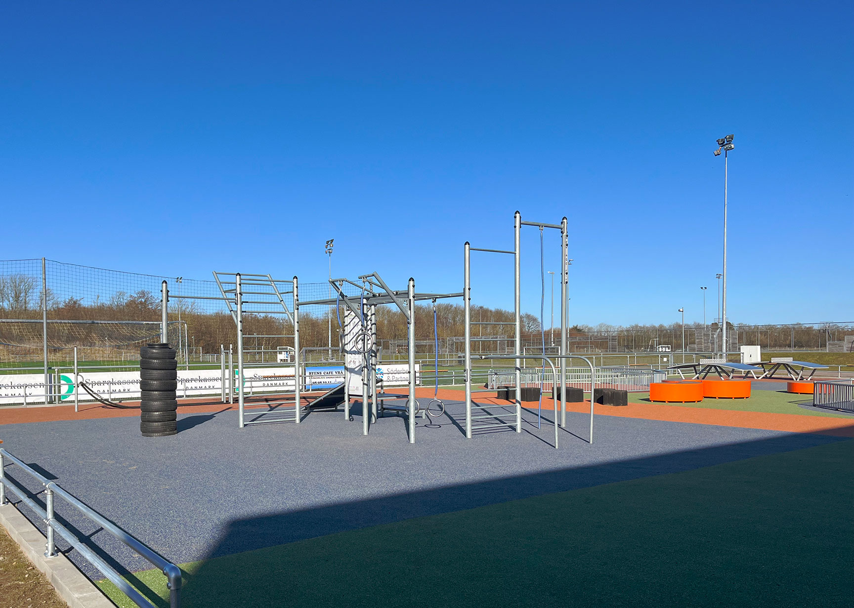 Utegym på grått underlag med orange parkmöbler i bakgrunden.